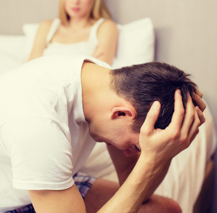man sitting on the bed with woman on the back hotel, travel, relationships, and sexual problems concept - upset man sitting on the bed with woman on the back